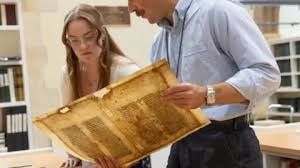 Archivist holding an aged vellum manuscript fragment with visible Latin text and frayed edges.