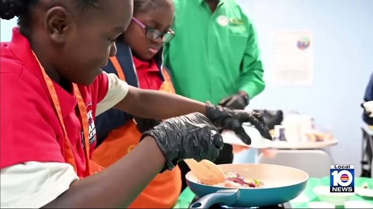 Dietitian Ashley Carter supervising children cooking a chicken and vegetable meal in a community kitchen.
