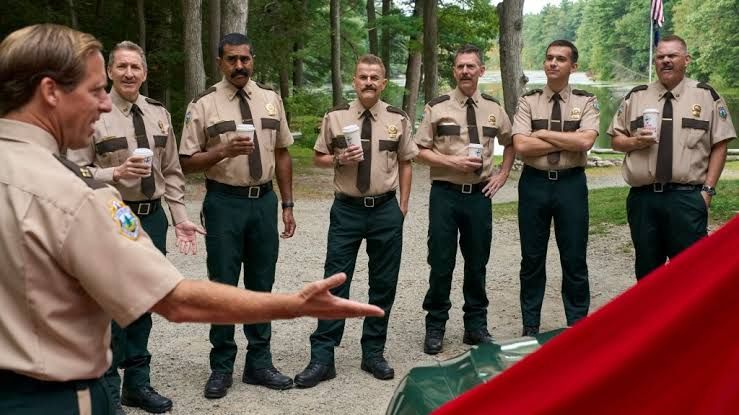 Cast members of Super Troopers 3 standing in police uniforms during a scene from the comedy film.