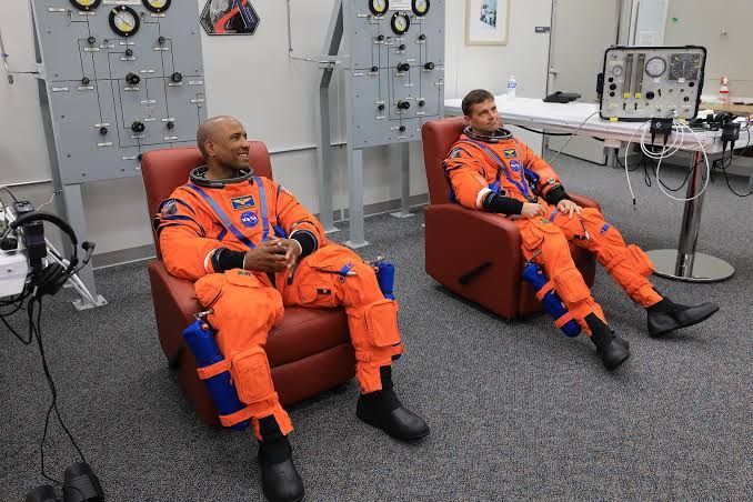 Astronauts Victor Glover and Reid Wiseman conduct spacesuit leak checks at Kennedy Space Center.