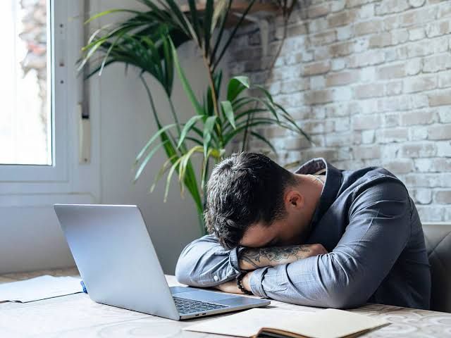 A man resting his head on a desk while working at a laptop, illustrating the focus on sleep and brain function.