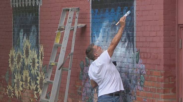Artist Jim Kiselica painting a new floral mural on the exterior brick wall of Parkleigh on Park Avenue in Rochester.