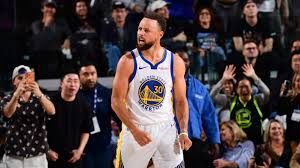 Stephen Curry standing at a press event in front of a basketball display.