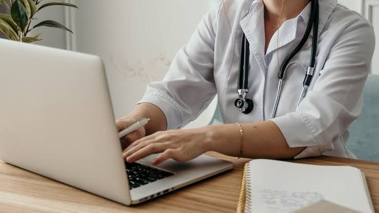 A doctor sitting at a computer terminal in a medical office to manage electronic patient health records.
