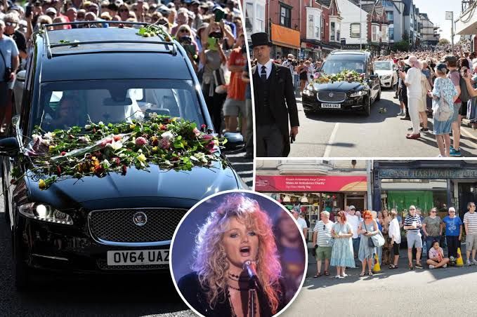 Hearse carrying Bonnie Tyler's coffin draped in a Welsh flag driving through a crowd of mourners in Wales.