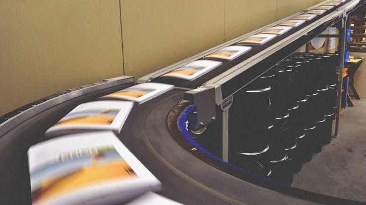 A business owner in a printing facility inspecting a large industrial book printing machine.