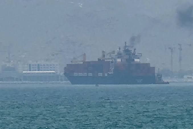 Aerial view of a cargo ship navigating the narrow Strait of Hormuz near the Iranian coastline.