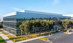 Modern glass office building with trees and landscaping under a blue sky in the Irvine Healthcare Corridor.