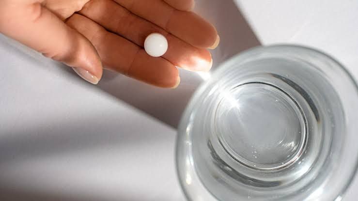 A person holds a single white pill and a glass of water, representing the new oral medication for cholesterol management.
