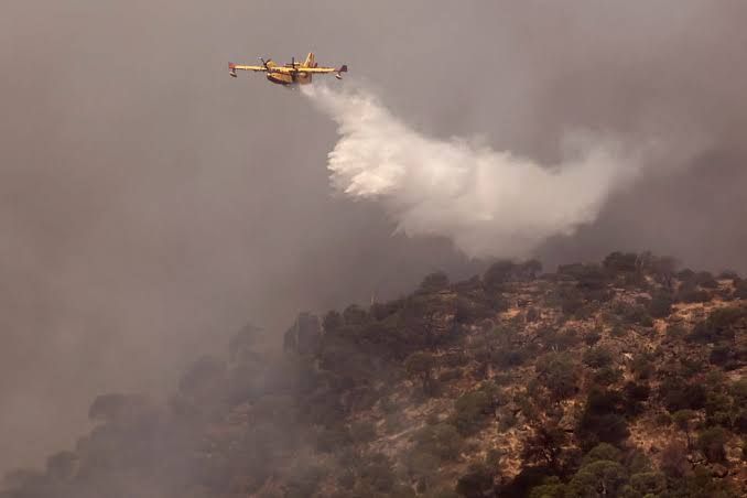 An aircraft drops water on a wildfire burning near Pelayos de la Presa, west of Madrid, during the July 2026 emergency.