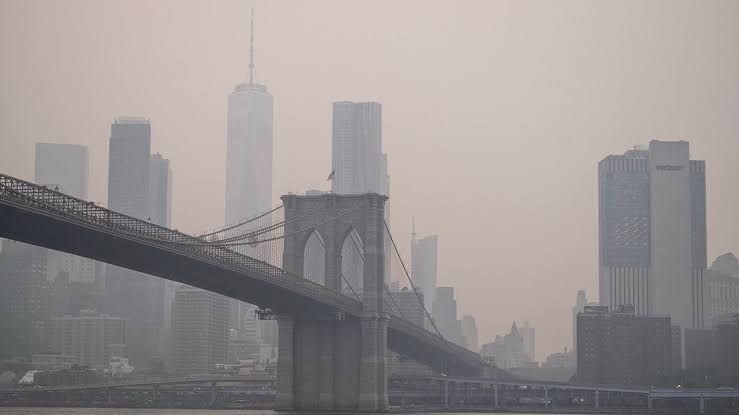 A woman wearing a face mask walks through New York City as smoke from Canadian wildfires obscures the skyline.