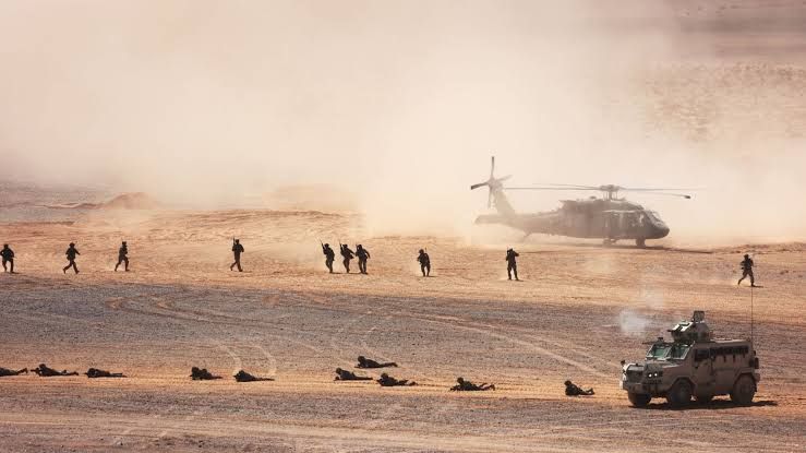 U.S. and Jordanian soldiers standing near a helicopter during a joint training exercise in the desert.