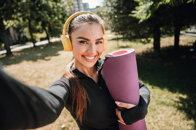 Young woman in athletic wear sitting on a yoga mat smiling outdoors.