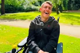 Jake Smith, a photographer with cerebral palsy, laughing while holding a camera in a park setting.