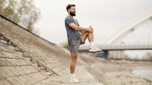 A man in athletic wear balancing on one leg outdoors while holding his knee to improve balance and leg strength.