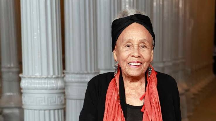 Betye Saar stands at the Los Angeles County Museum of Art, posed near her complex mixed-media assemblage artworks.