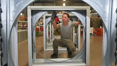 Factory worker assembling steel parts on a wind turbine frame in a manufacturing plant.