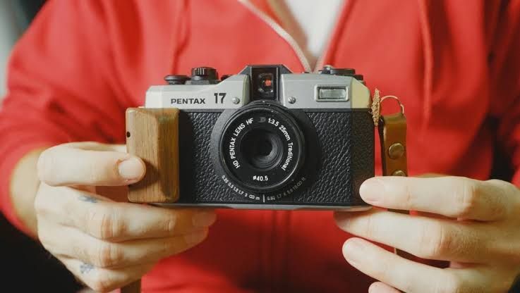 A silver and black Pentax 17 film camera sitting on a wooden surface.