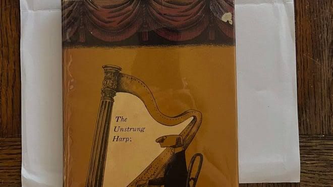 A vintage Edward Gorey book with an apology note and a hundred dollar bill resting on a bookstore counter.