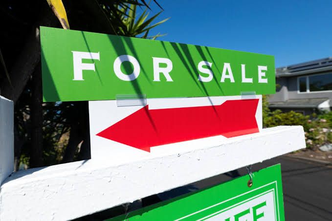 A For Sale sign stands in front of a residential house in California under a clear sky.