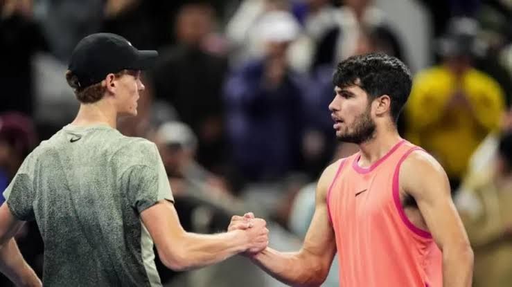 Carlos Alcaraz and Jannik Sinner playing on a hard court during a professional tennis match.