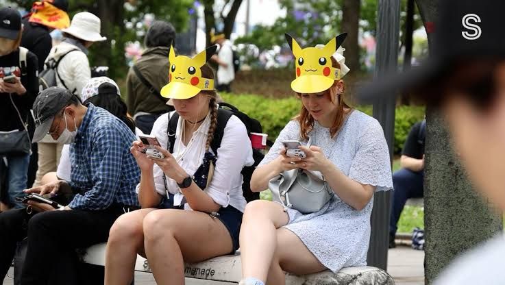 A group of players in an Auckland park looking at their phones while participating in a Pokemon Go raid event.