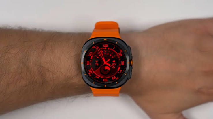 Close up of a Samsung Galaxy Watch Ultra screen displaying a red clock face in a dim room.
