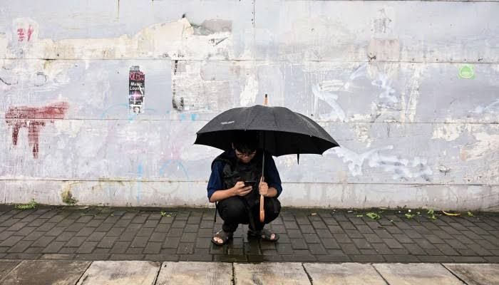 A resident in Yangon uses a mobile phone during a storm, representing the millions reliant on satellite internet in Myanmar.