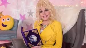 Dolly Parton holding a children's book while wearing a bright yellow suit and colorful jewelry.