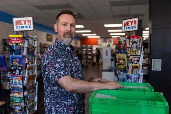 Marc Bowker, owner of Alter Ego Comics, inspects a bin of comics surrounded by superhero displays in his Lima shop.