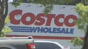 A Costco warehouse entrance with a sign promoting health services next to a SCAN Health Plan medical representative.