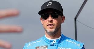 Denny Hamlin wearing his team gear while talking to the media about NASCAR vehicle changes.