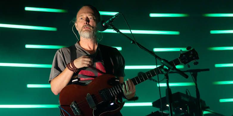 Thom Yorke performing on stage during a solo concert with his guitar and effects pedals.