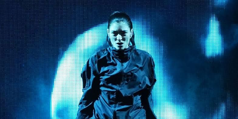 Lorde performing on stage with dramatic lighting during a concert event.