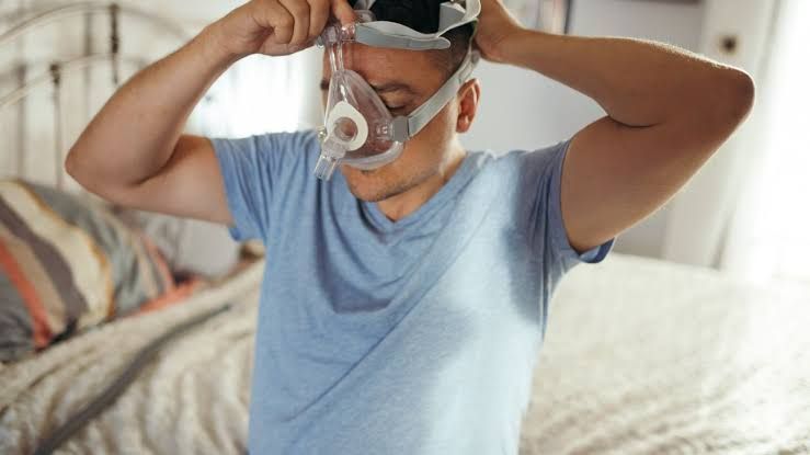 A man adjusting his CPAP mask to manage sleep apnea symptoms.