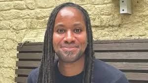 Professor Jason Arday sitting on a wooden bench at the Cambridge University Faculty of Education.