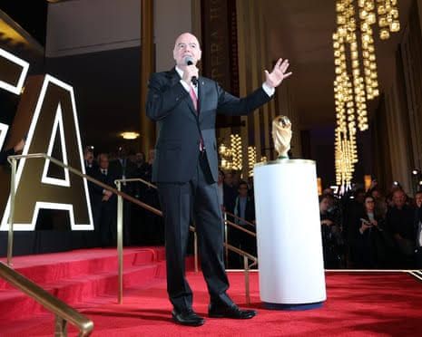 Gianni Infantino stands at the 2026 World Cup draw in New York with the trophy on a plinth nearby.