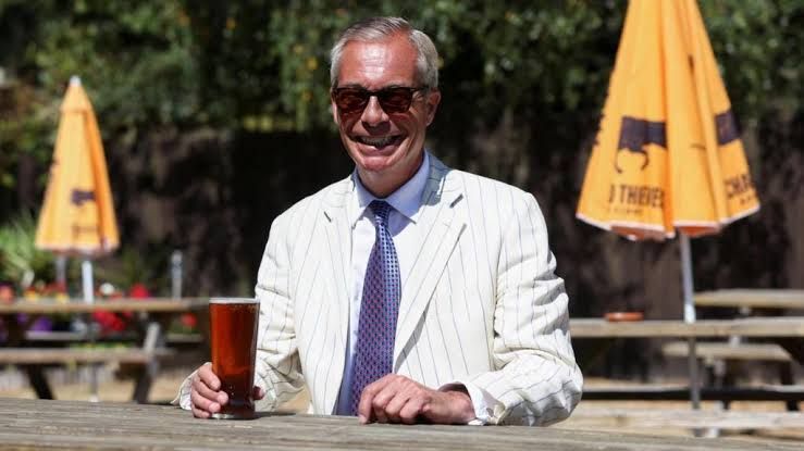 Nigel Farage standing in Clacton on election day wearing a white suit and sunglasses.