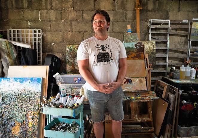 Artist Josh Hoffman standing beside his award-winning painting Roots #2 at an exhibition in Dormont.