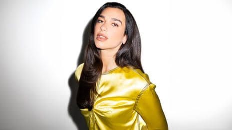 Dua Lipa stands in a gold dress while attending a public event in London.