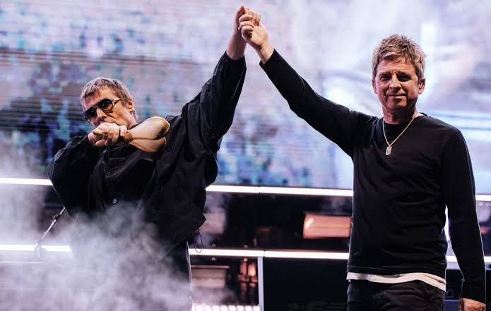 Noel and Liam Gallagher standing on a large concert stage during a soundcheck before a massive stadium show.