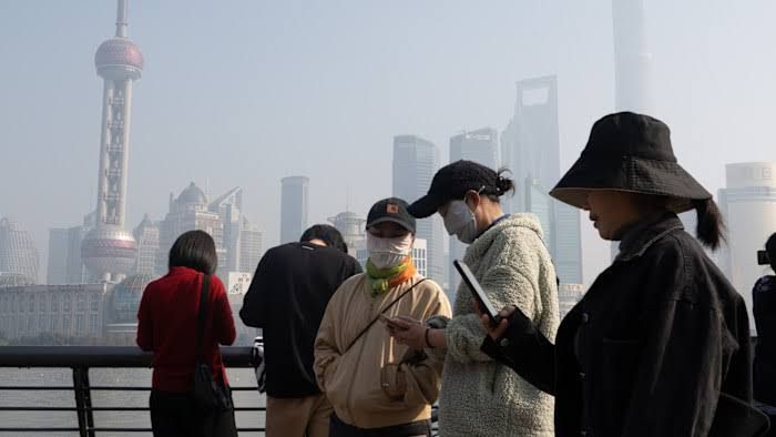 Industrial chimneys emitting smoke in an urban area in China against a hazy, polluted skyline.