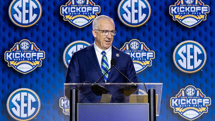 SEC Commissioner Greg Sankey speaking at a podium during the SEC Football Media Day in Tampa.