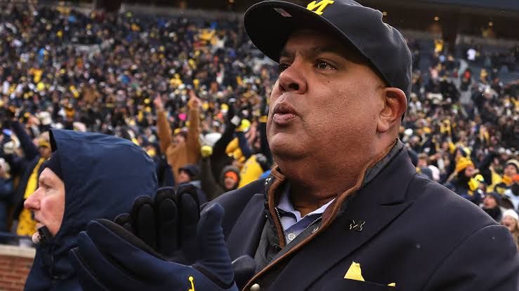 Warde Manuel standing during a press event representing the University of Michigan athletics department.