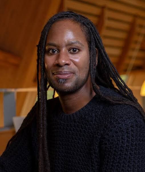 Professor Jason Arday stands in a library setting at the University of Cambridge during an academic lecture.