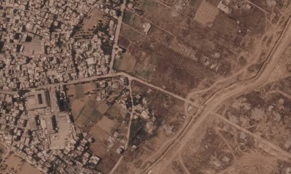 Satellite view of a long, dark earthen berm cutting through demolished infrastructure in the Gaza Strip.