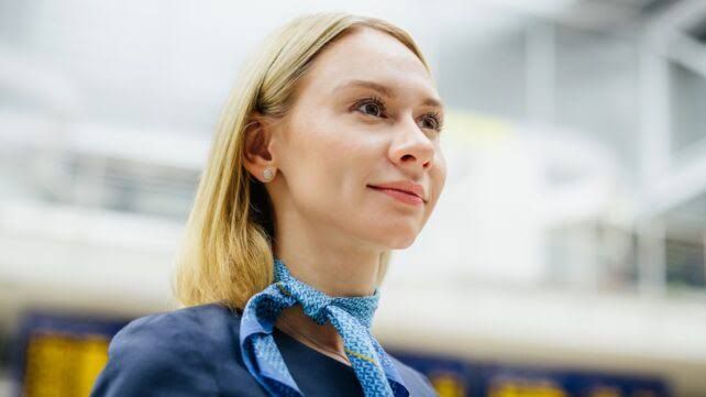 Flight attendant working in an airplane cabin while cruising at high altitude during daylight.