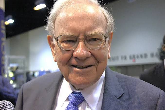 Warren Buffett sitting in a chair during an annual shareholder meeting while discussing market principles.