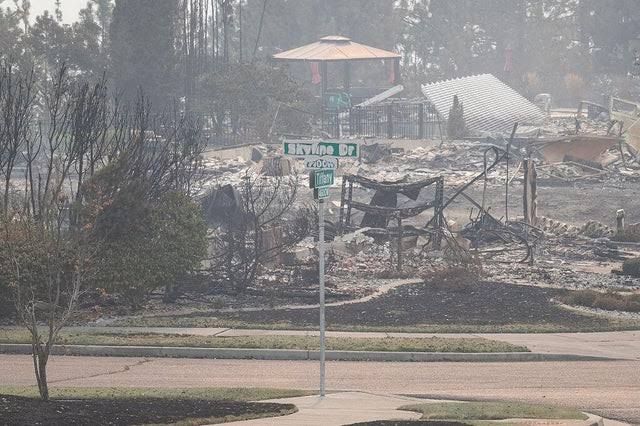 A partially melted street sign stands before a ruined residential house in Spokane, Washington after a wildfire.