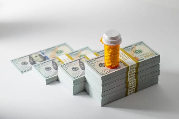 Prescription bottle and pills on stacks of $100 bills representing rising medical inflation costs.